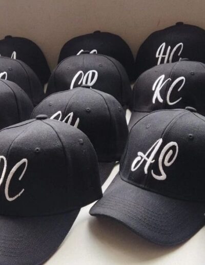 Gorras negras bordadas con iniciales blancas en cursiva, personalización elegante para evento empresarial