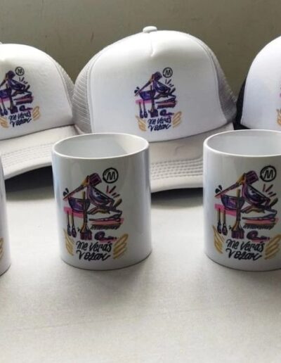 Gorras de camionero y mugs blancos con diseño 'Me Verás Volar' para evento de coaching, souvenirs promocionales.